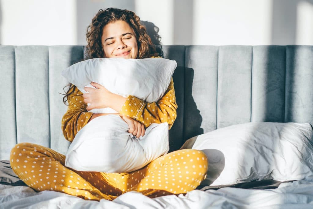 Woman in yellow pajamas hugging pillow and smiling.